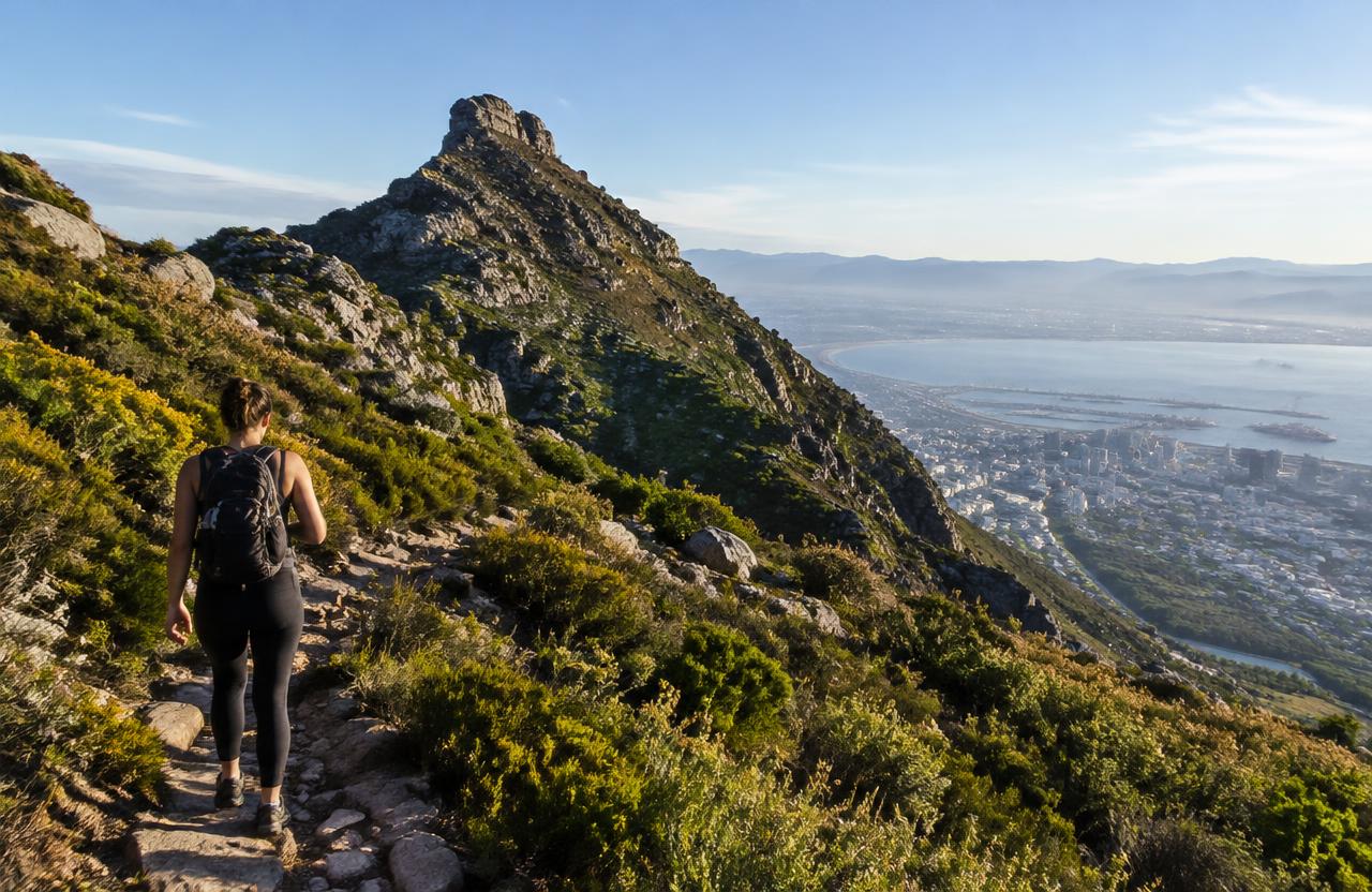 Hiker on a fynbos trail on Devil's Peak with the city and bay below